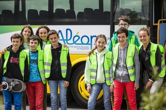 Huit collégiens avec des gilets haute visibilité verts devant un car scolaire ALEOP